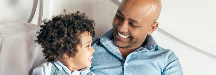 A father and son share a joyful moment, smiling and looking at each other while sitting close together.